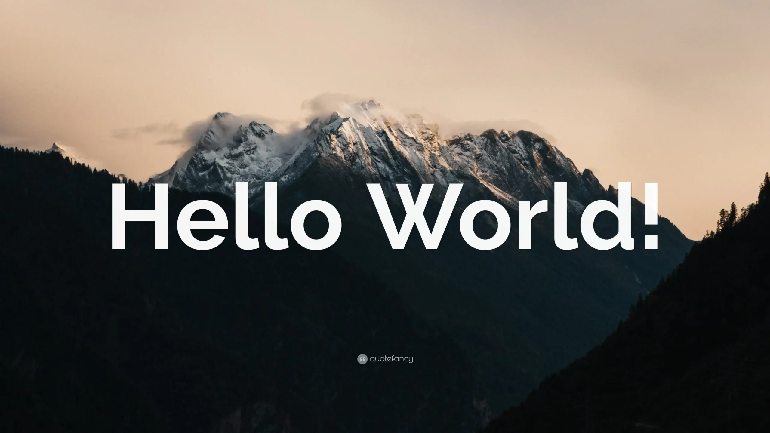 The words "Hello World!" in a bold, white sans-serif font are superimposed over a landscape photo of snow-capped mountains and dark green forests. The mountains are bathed in a warm, golden light from what appears to be a sunrise or sunset, while the foreground and sides of the image are dominated by the dark, shadowy peaks of forested hills. A small, faint watermark that reads "quotefancy.com" is visible in the bottom center.